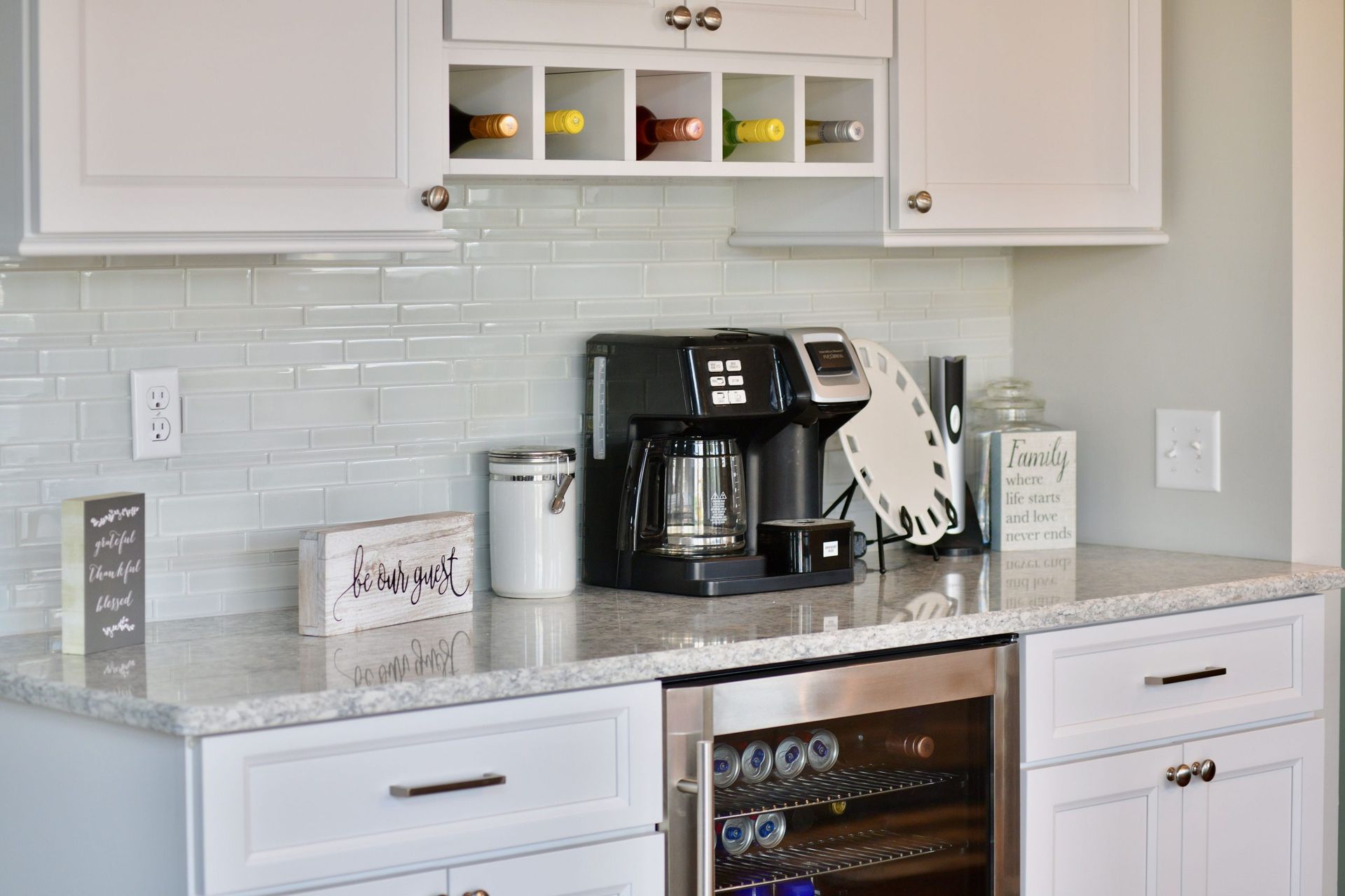 A kitchen with white cabinets , a coffee maker , and a wine cooler.