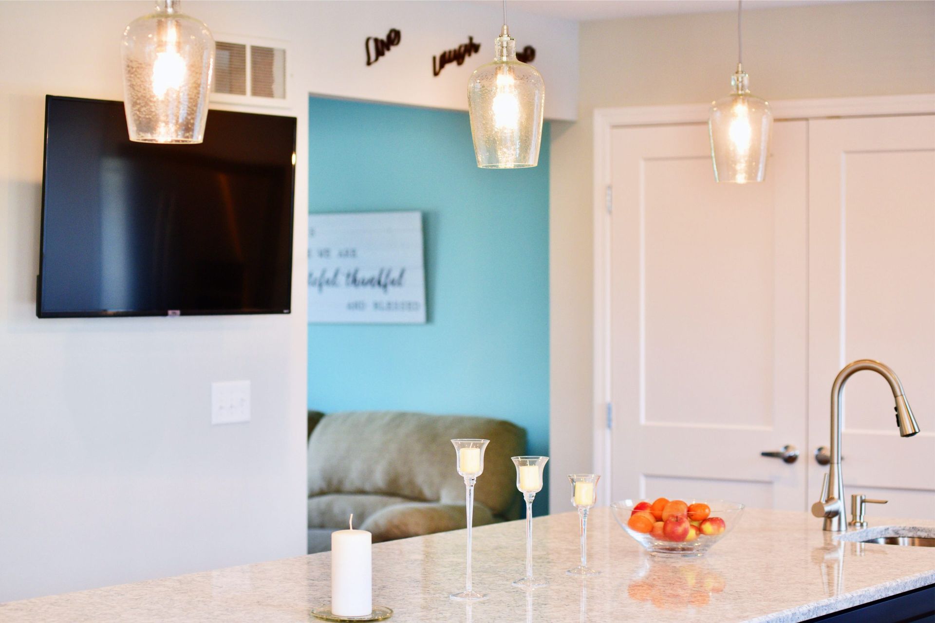 A kitchen with a tv on the wall and a couch in the background.