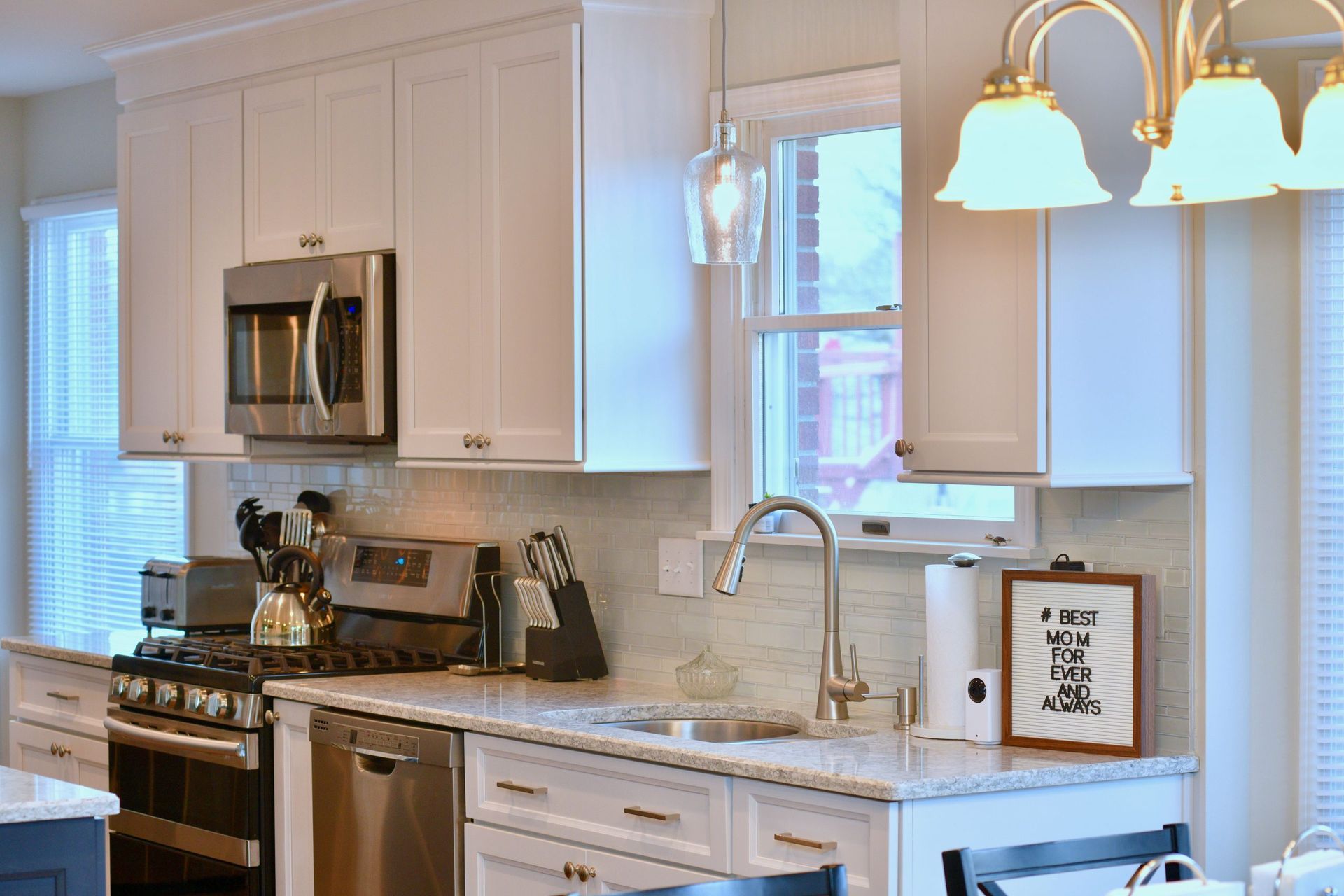 A kitchen with white cabinets , stainless steel appliances , a sink , stove and microwave.