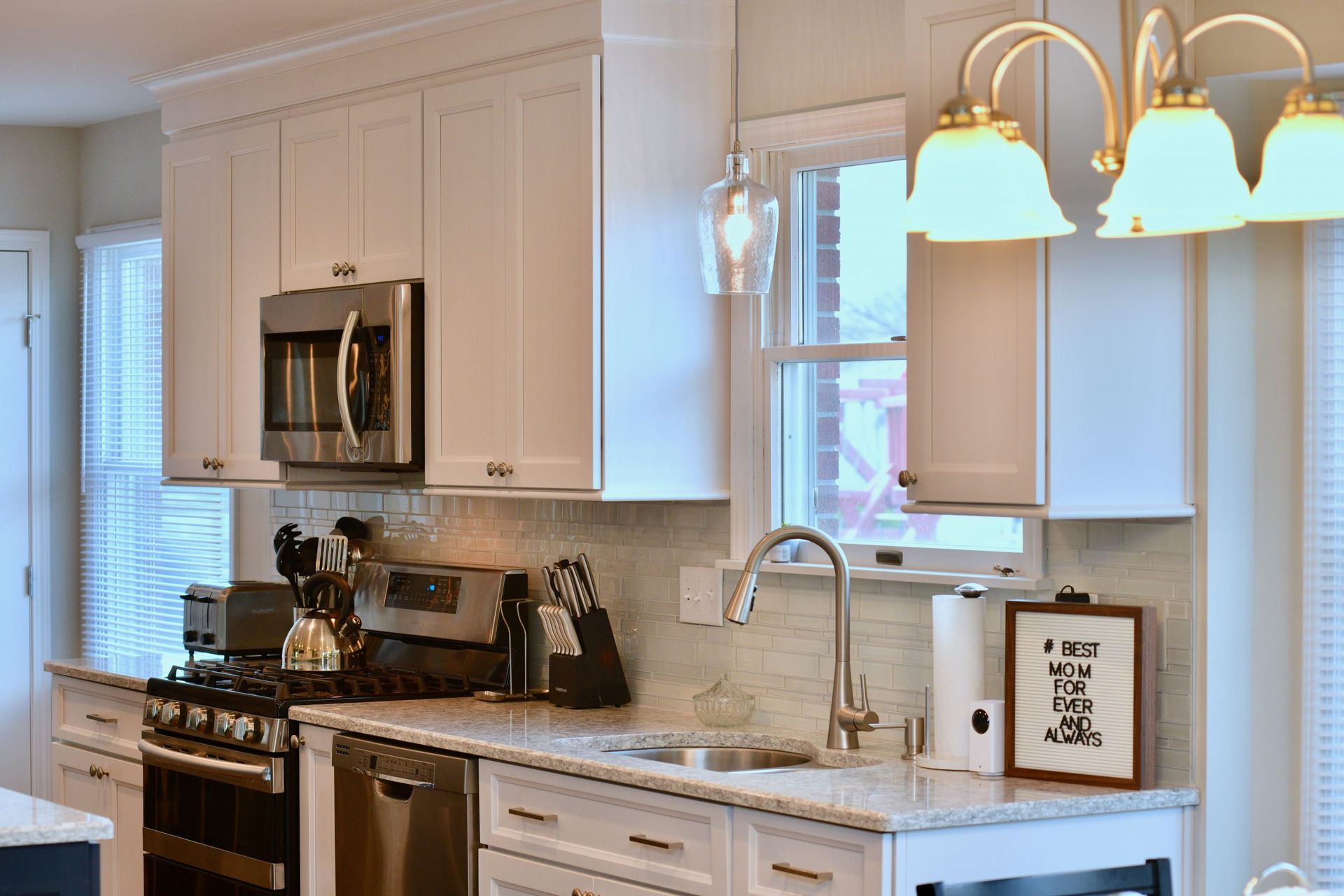 A kitchen with white cabinets , stainless steel appliances , a sink , and a window.