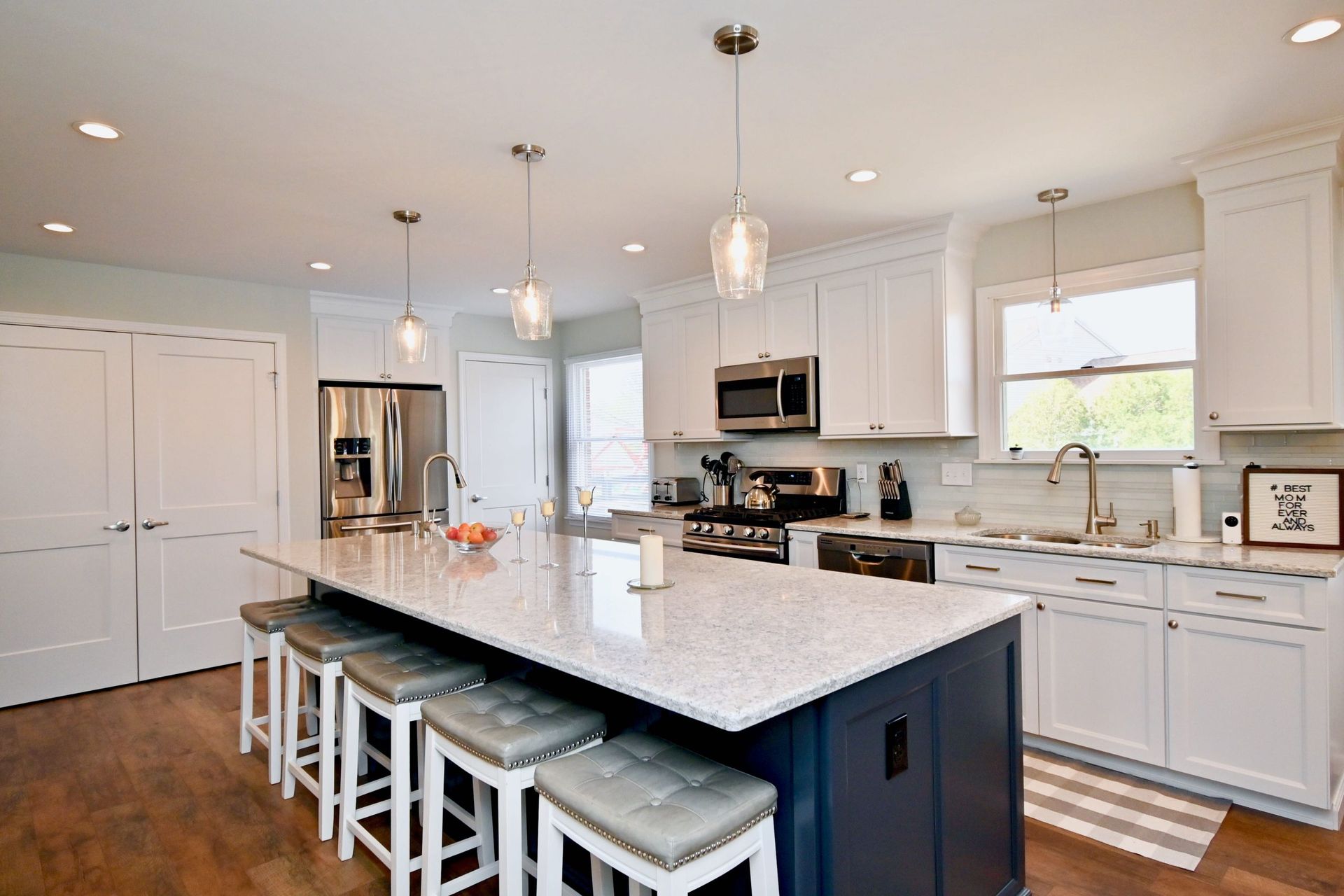 A kitchen with white cabinets , granite counter tops , stools and a large island.