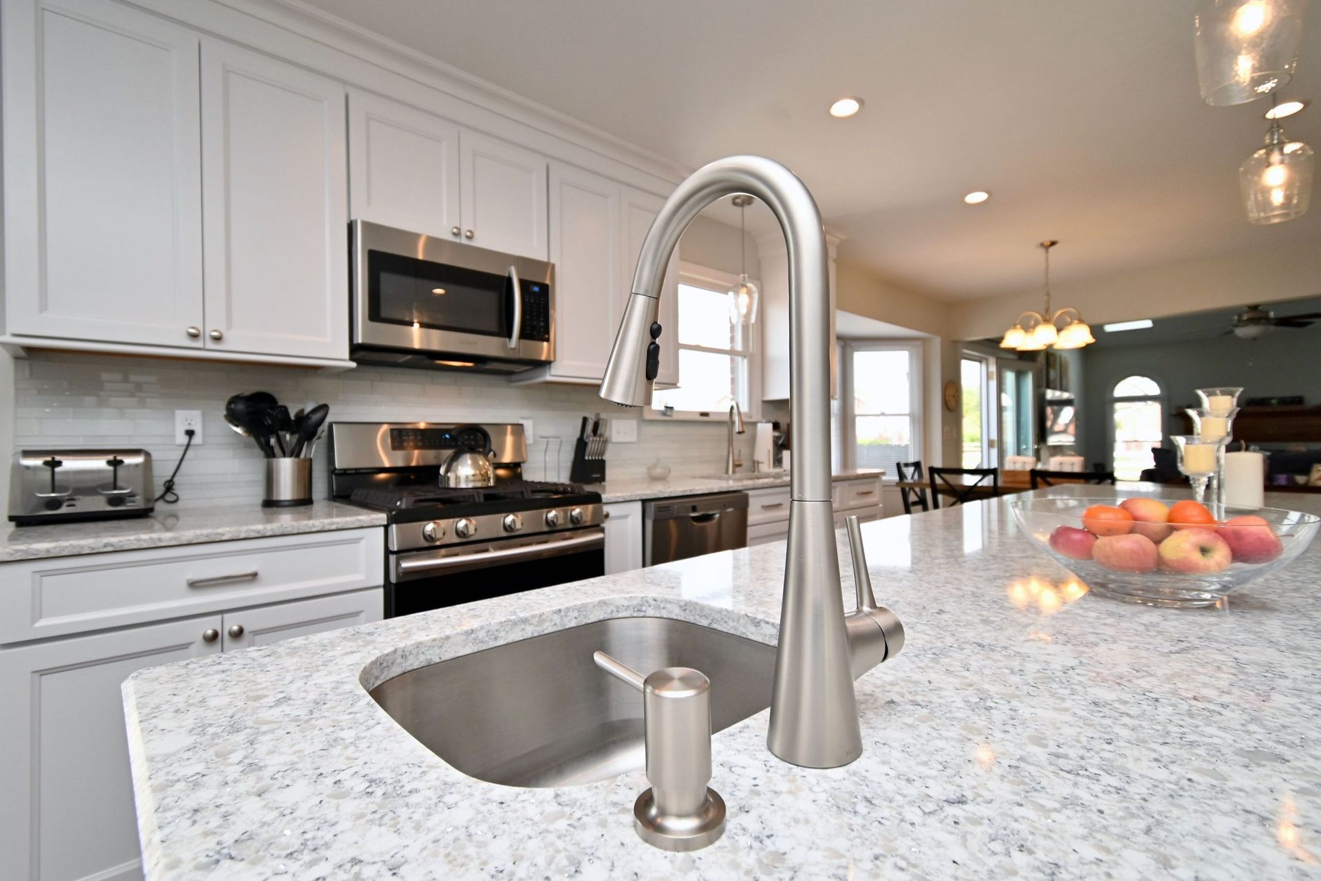 A kitchen with a sink , stove , microwave and a bowl of fruit on the counter.