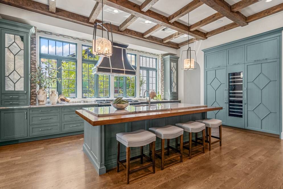 A kitchen with blue cabinets , a large island , stools and a refrigerator.