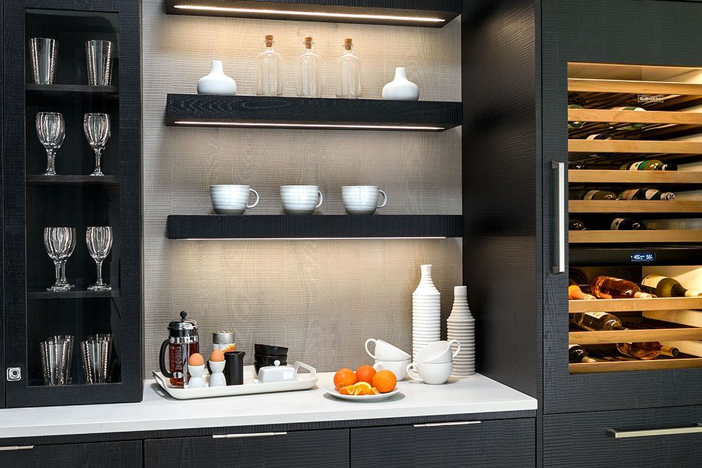 A kitchen with a wine cooler and shelves with cups and glasses on them
