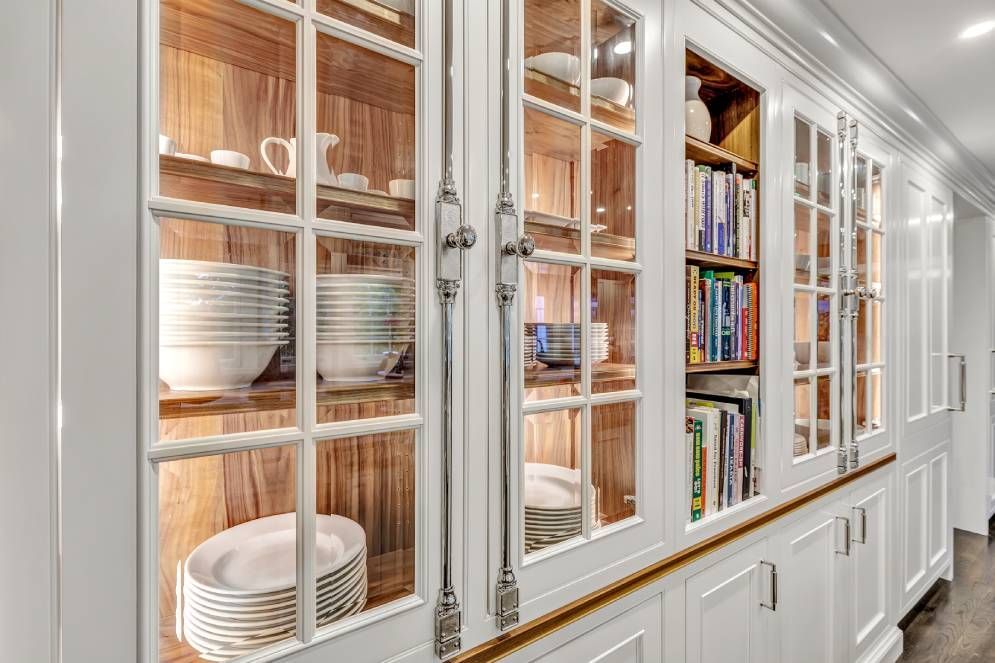 A kitchen with white cabinets and glass doors filled with dishes and books.