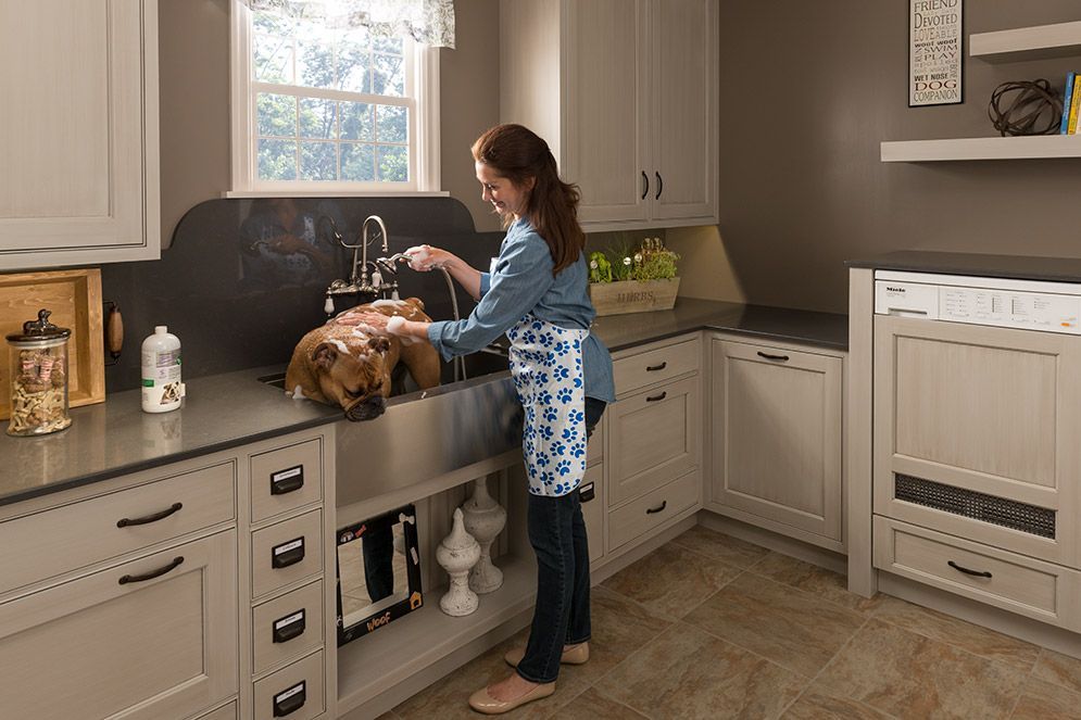 A woman is washing a dog in a kitchen sink.