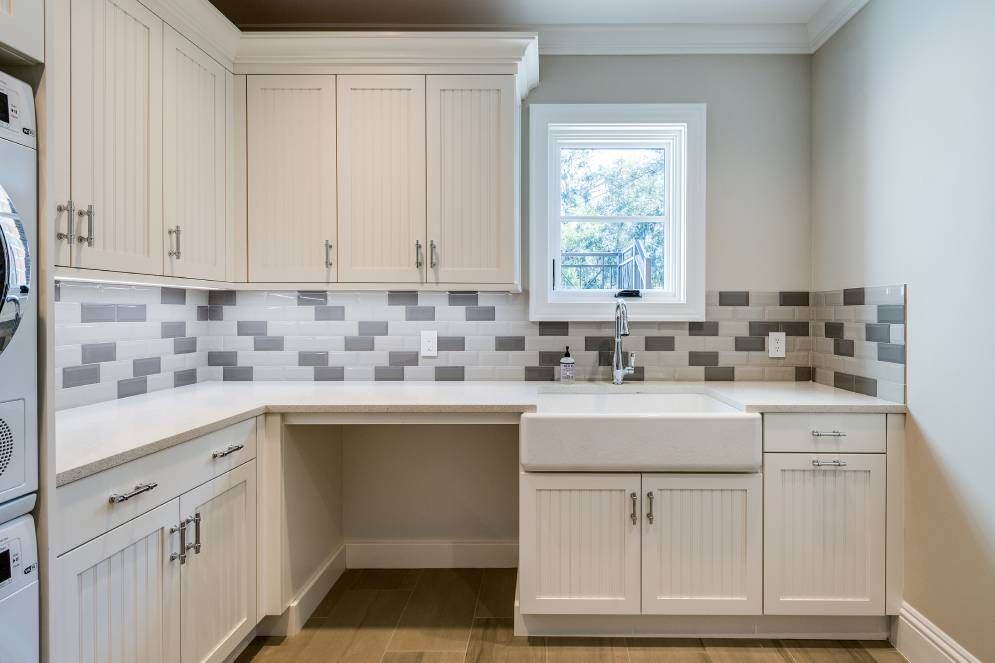 A laundry room with white cabinets , a sink , a washer and dryer , and a window.