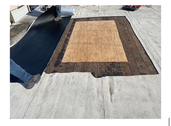 Workers installing roofing underlayment and plywood on a flat roof