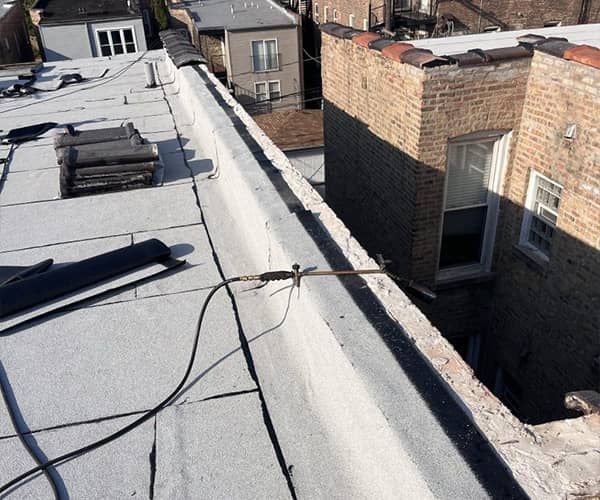 Rooftop with white coating, black cables, and brick chimneys beside neighboring buildings