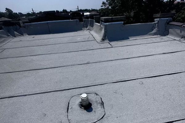 Flat rooftop with white membrane, vents, and parapet walls under a clear sky.