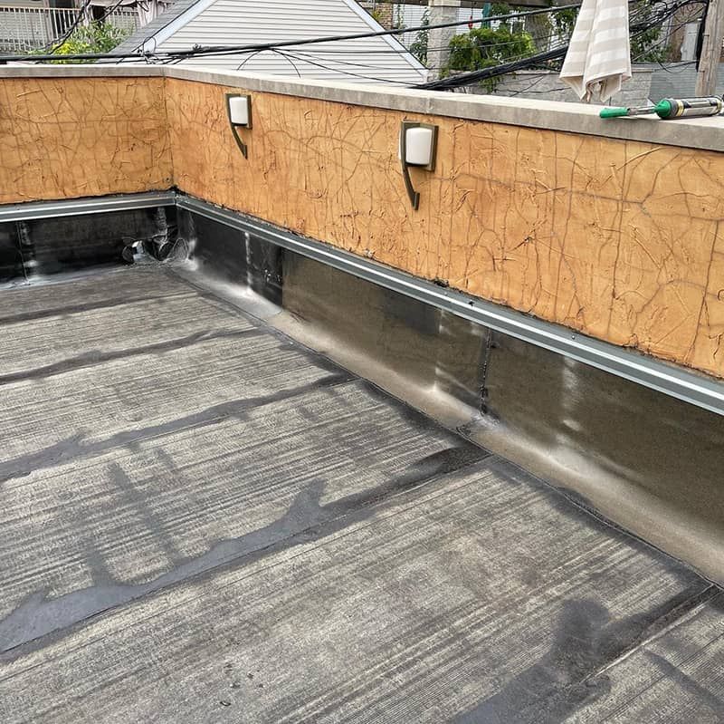 Rooftop with black waterproofing membrane and tan parapet wall under bright daylight.