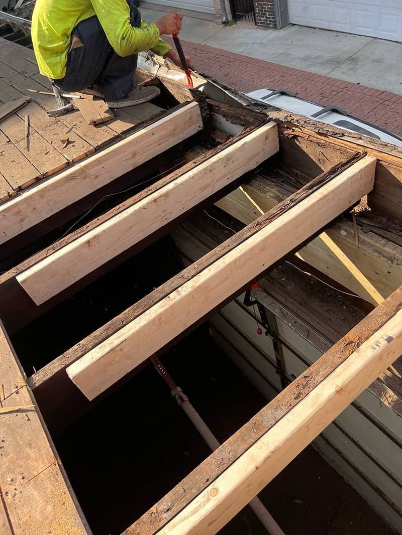 Worker repairing roof framing with exposed wooden beams and an open roof section