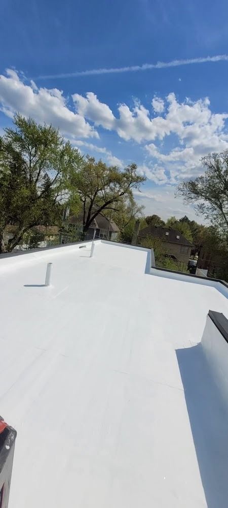 White rooftop under a bright blue sky with clouds and trees in the background