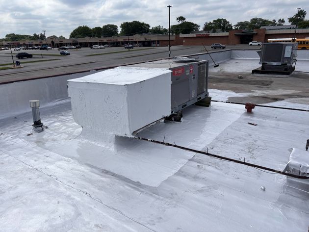 White rooftop HVAC unit on a flat commercial roof with wet patches and overcast sky.