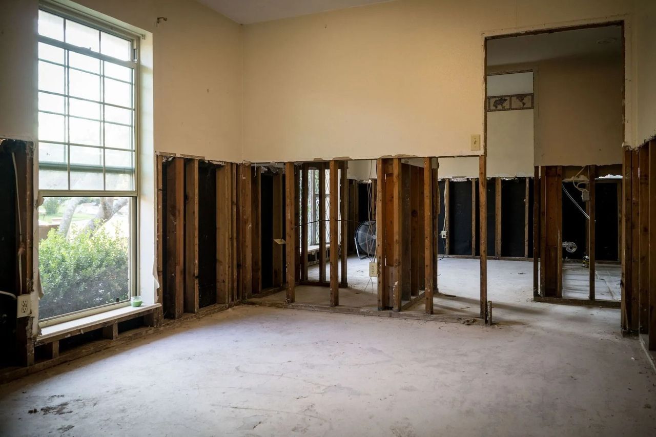 Empty room undergoing renovation with exposed wooden framing and large window.