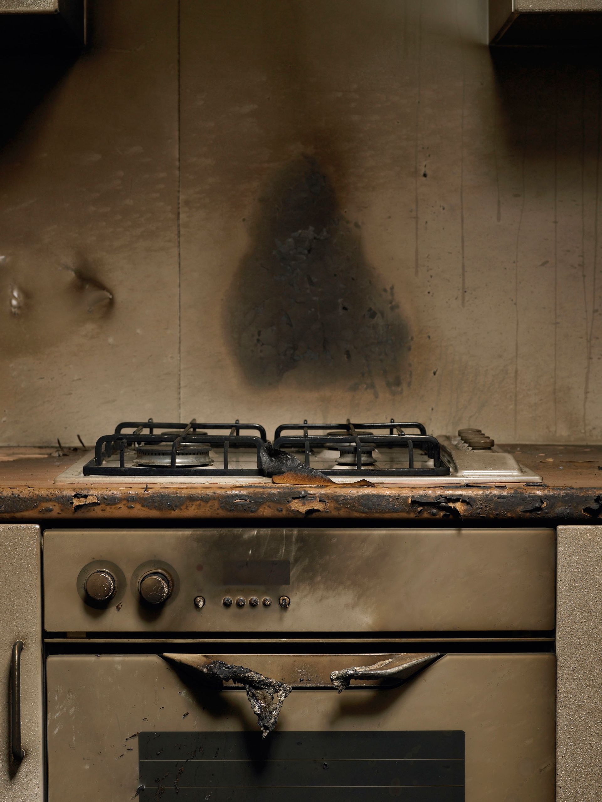 Burnt kitchen, gas stove centered, soot on walls and cabinet, charring on oven door.