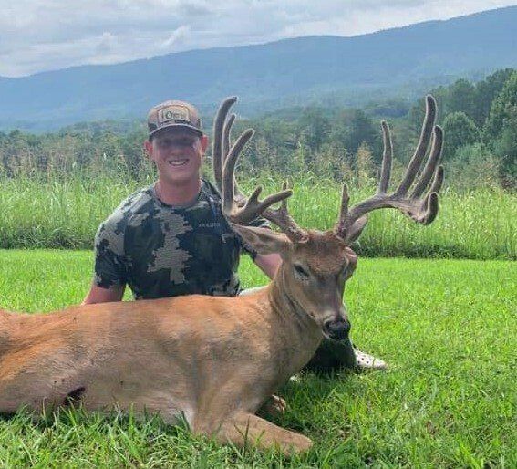 A man is kneeling next to a deer in the grass.