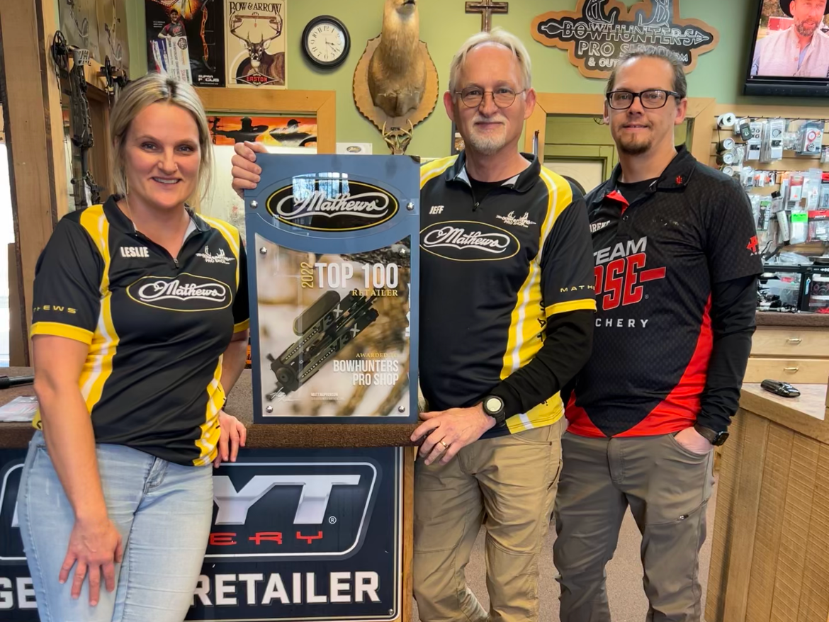 Three people are standing in front of a sign that says yt retailer