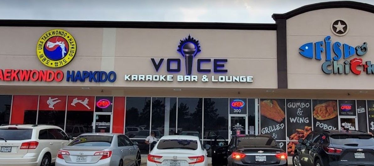 A karaoke bar and lounge with cars parked in front of it.