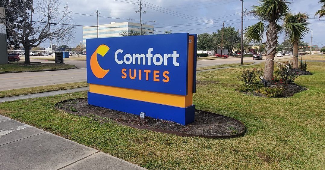 A blue and yellow comfort suites sign is sitting on the side of the road.