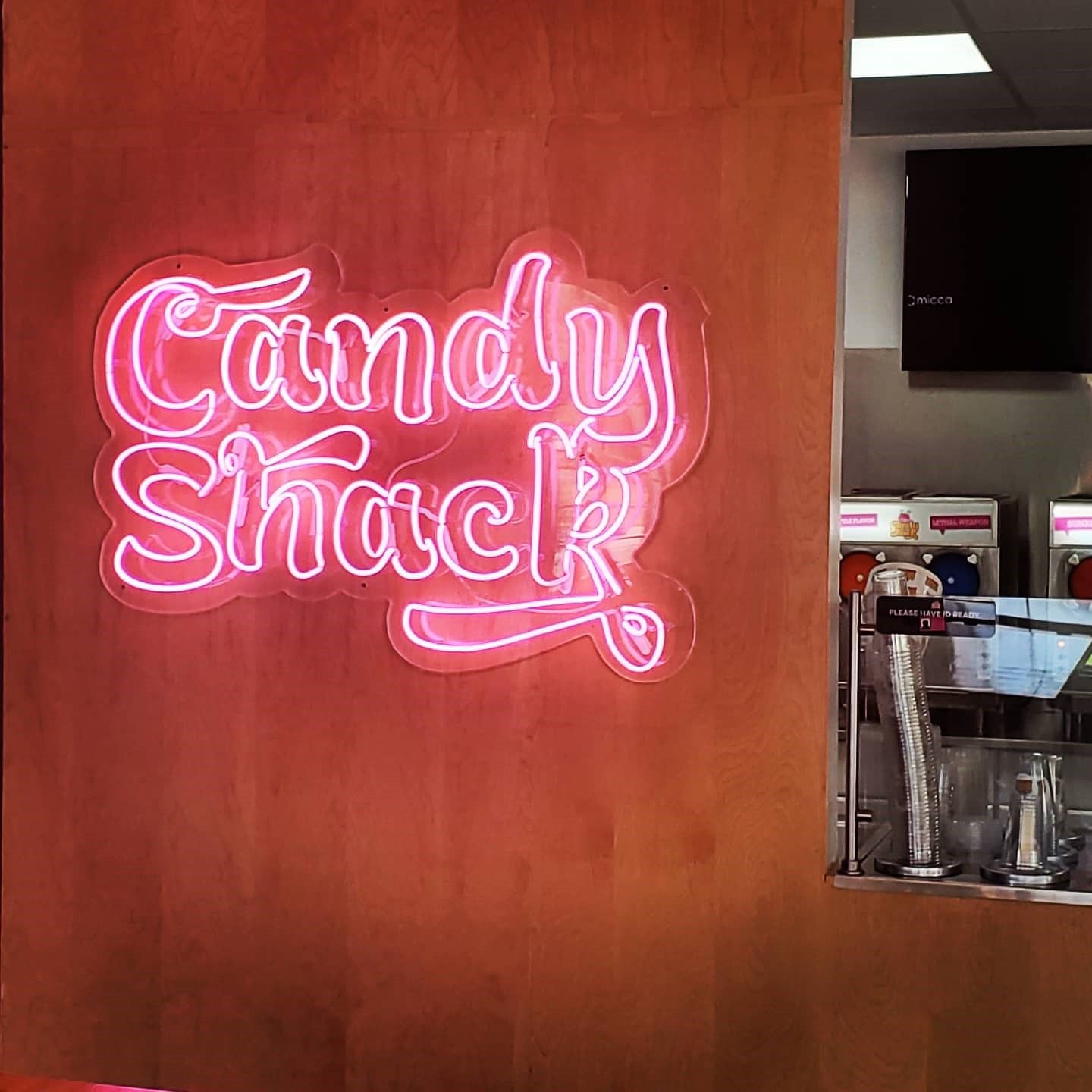A neon sign that says candy shack is on a wooden wall.