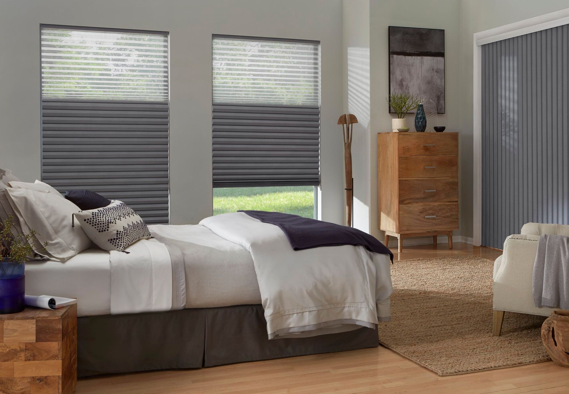 A bedroom with a bed , dresser , chair and window shades.