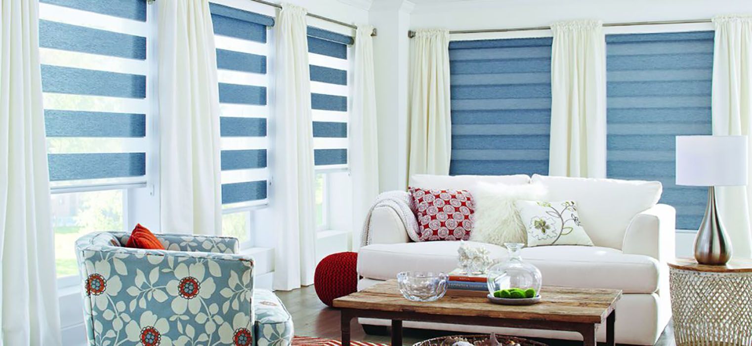 A living room with a white couch , chair , coffee table and blue blinds.