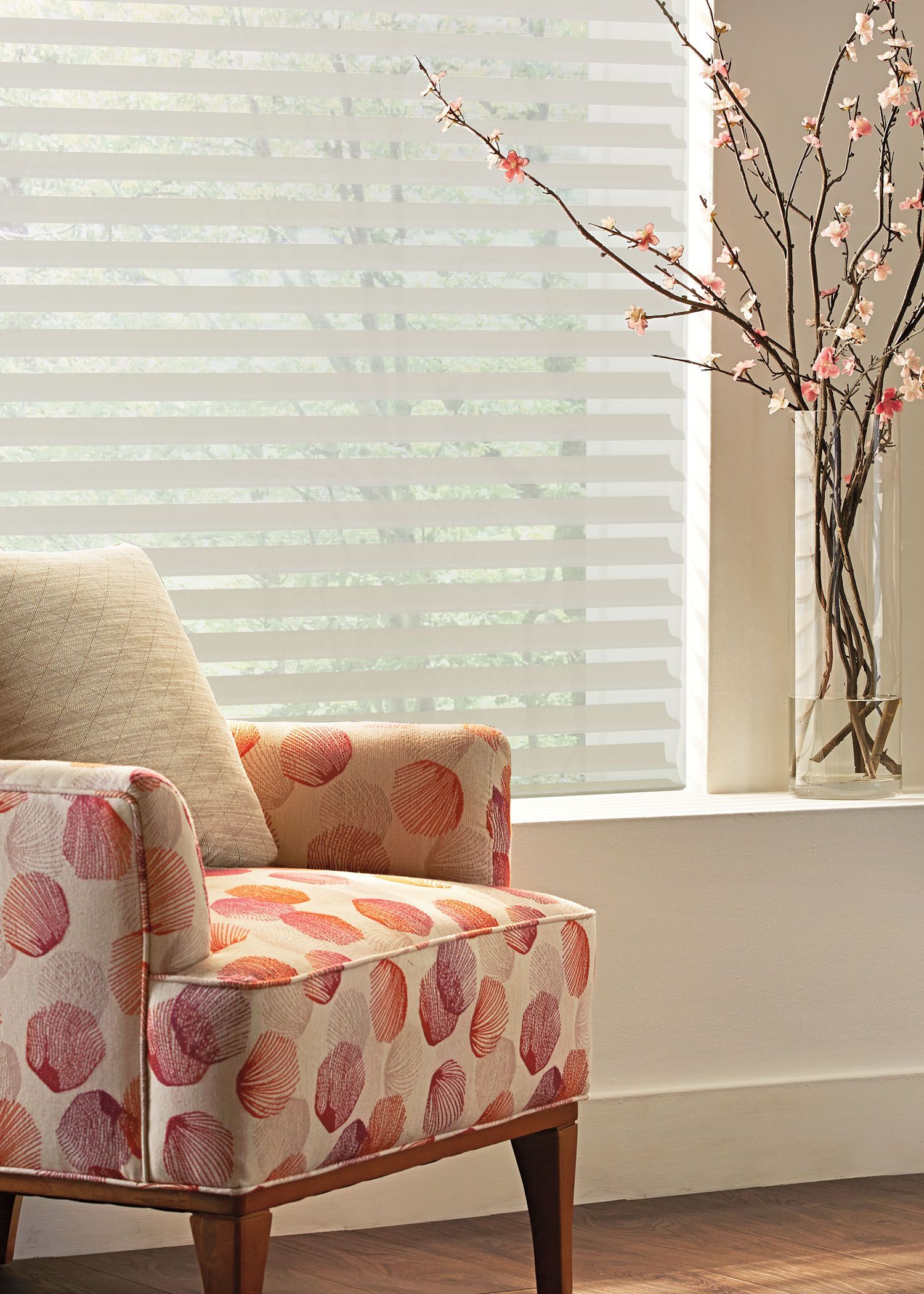 A chair is sitting in front of a window next to a vase of flowers.