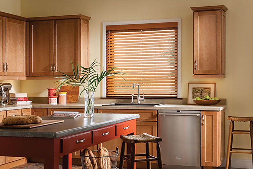 A kitchen with wooden cabinets , a sink , a dishwasher and a window with blinds.