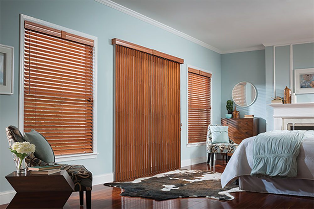 A bedroom with a bed , chair , table , fireplace and wooden blinds.