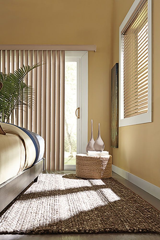 A bedroom with a bed , rug , blinds and a sliding glass door.