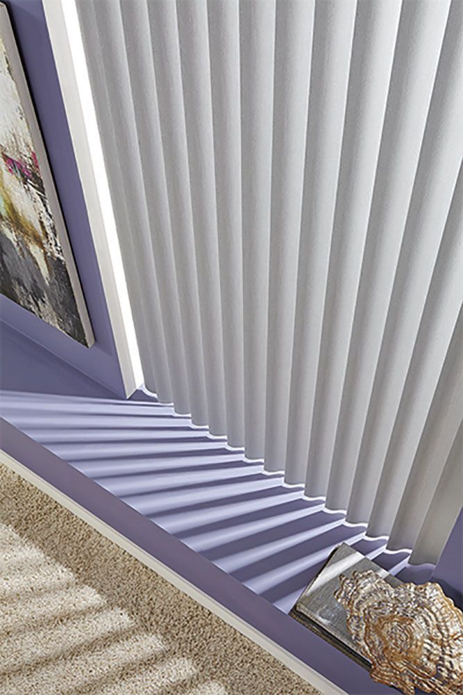A close up of a window with vertical blinds and a picture on the wall.