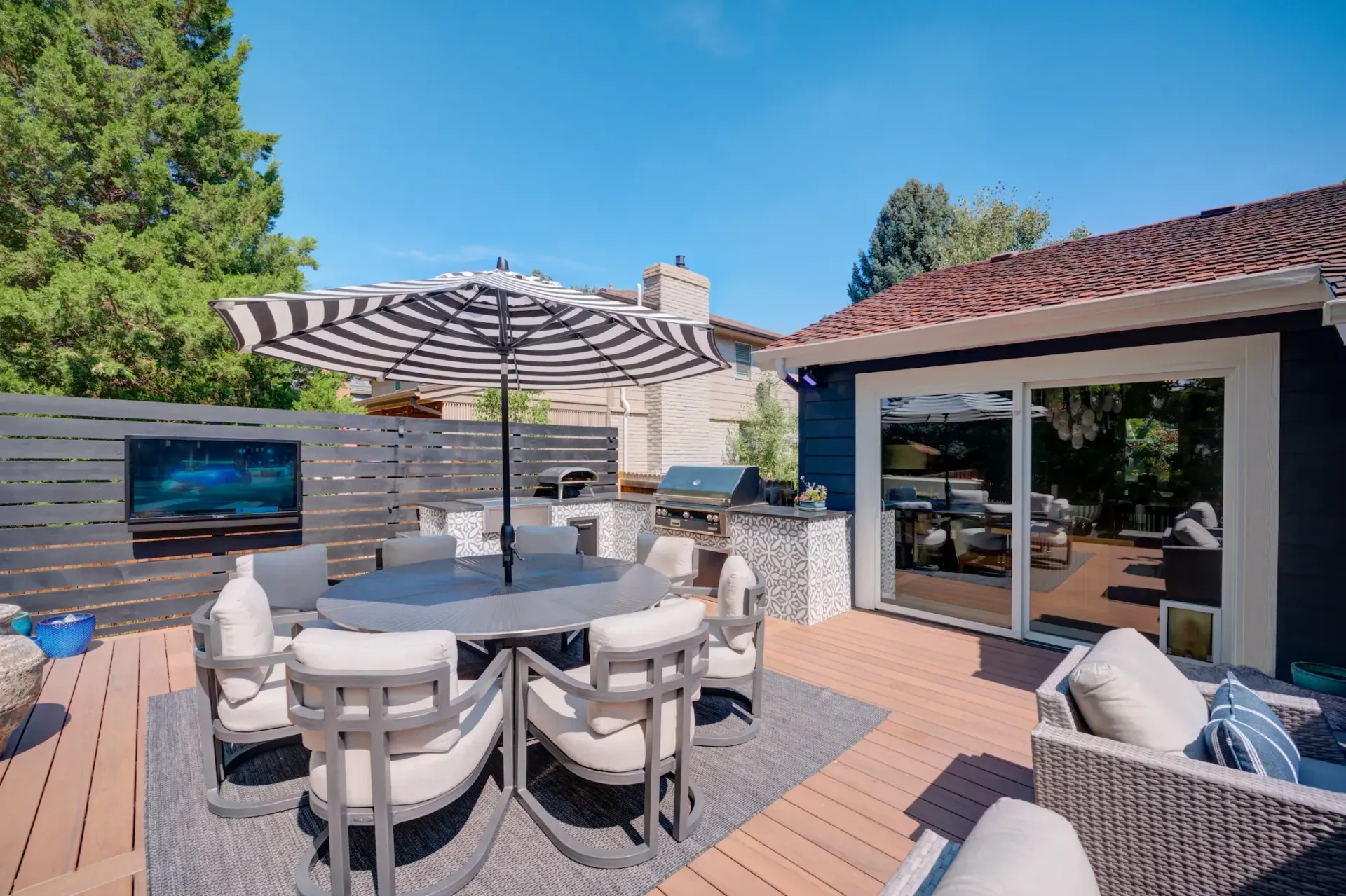 Patio with outdoor dining table, cushioned chairs, TV, and sliding glass doors under a red-tiled roof