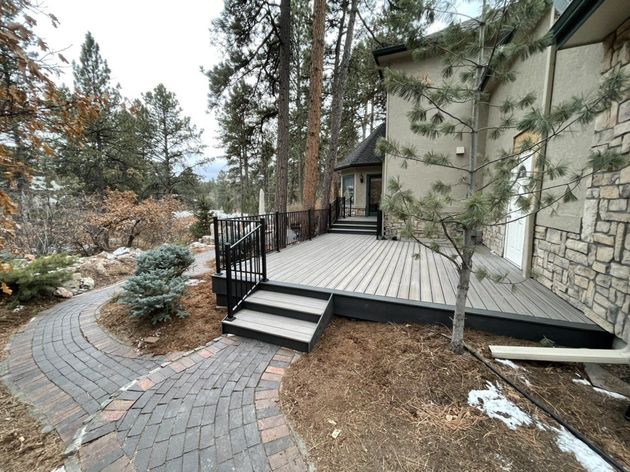 Curved brick walkway leading to a stone house porch with steps and trees in a wooded yard