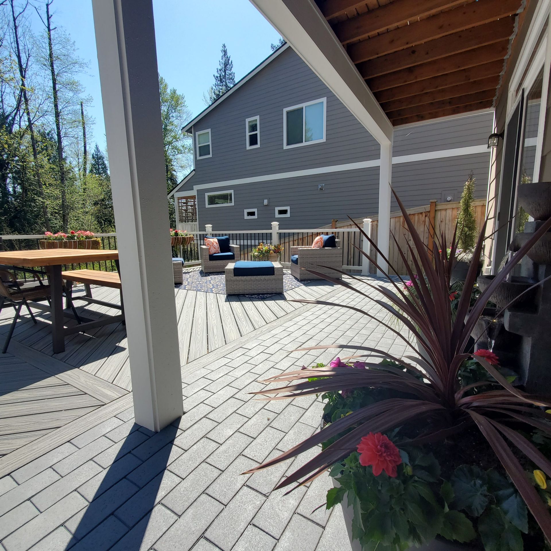 Sunlit backyard deck with white railings, outdoor seating, planter boxes, and a two-story gray house