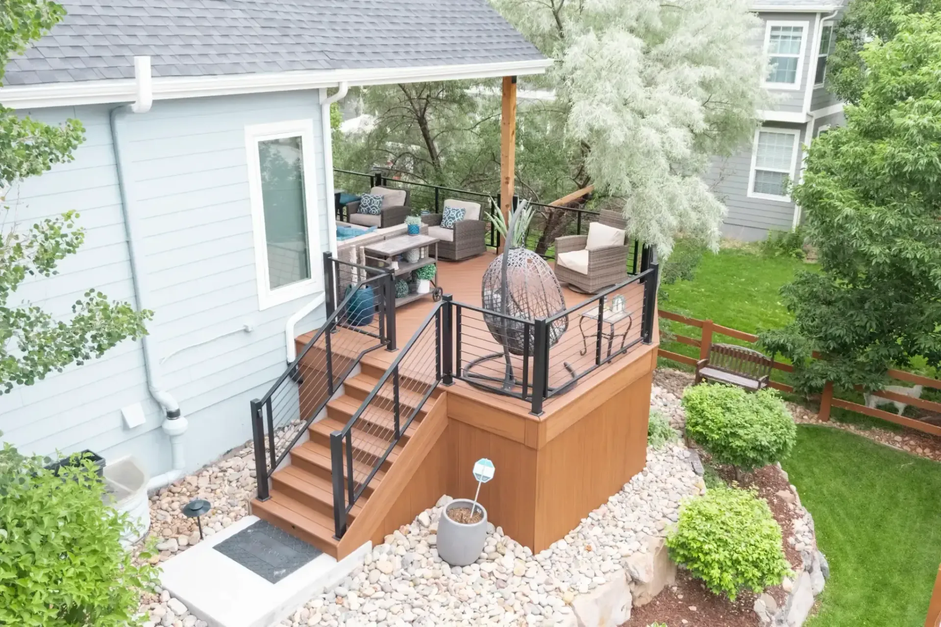 Back deck with stairs, patio furniture, and potted plants beside a white house