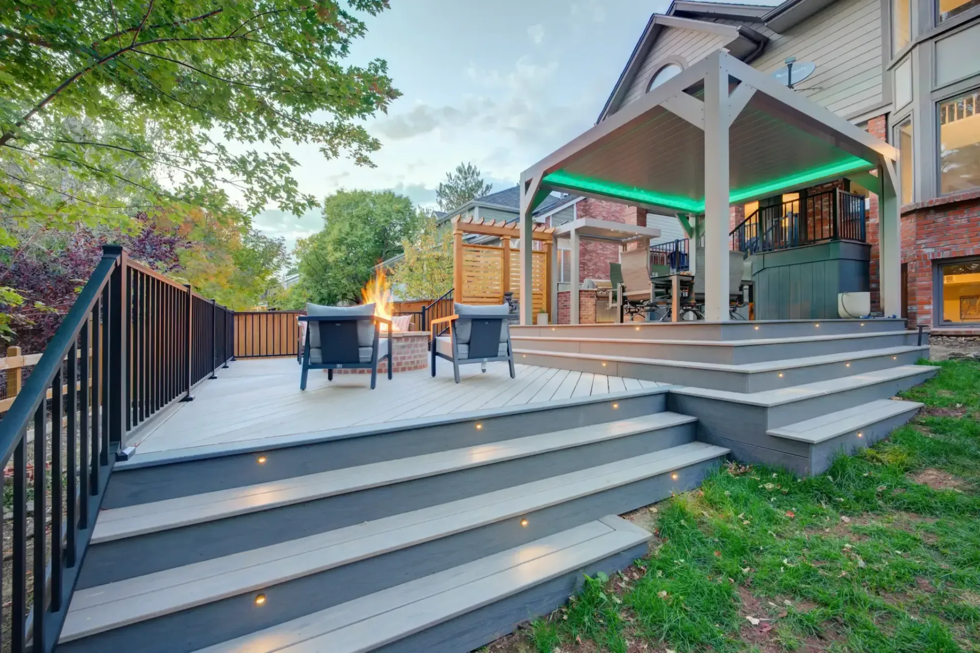 Outdoor patio with gray steps, black chairs, and a lit covered deck beside a house and trees
