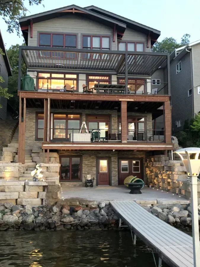 Lakefront house with three wooden decks and a dock over the water at dusk