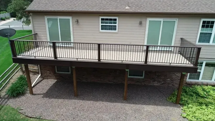 Wooden deck with railing attached to the back of a beige house, viewed from the yard.