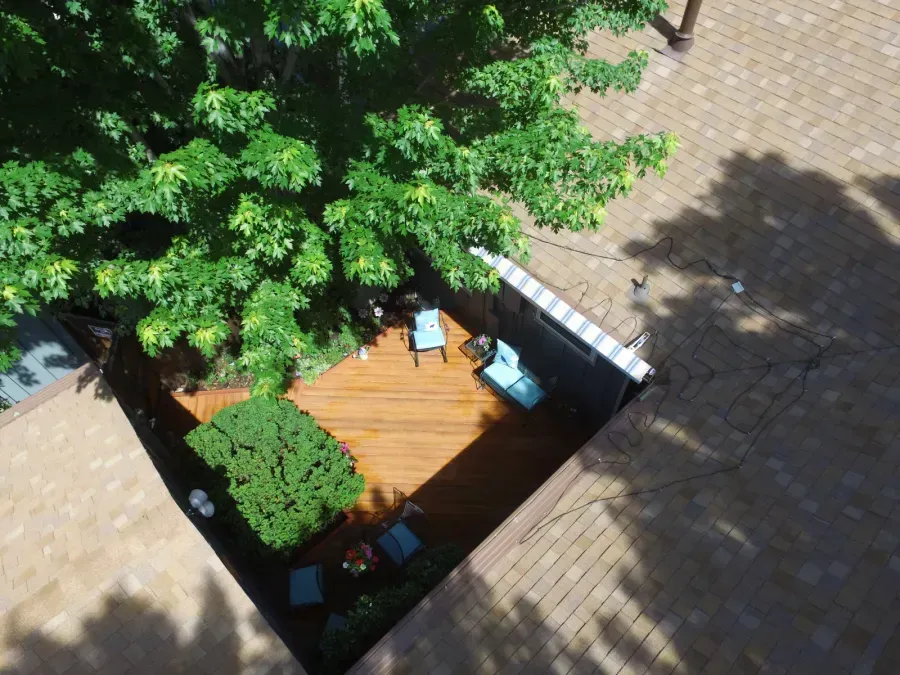 Small rooftop patio with wooden deck, blue chairs, and a large leafy tree casting shade.