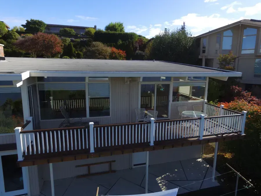 Modern house with a white-railed deck and covered patio in a landscaped hillside setting