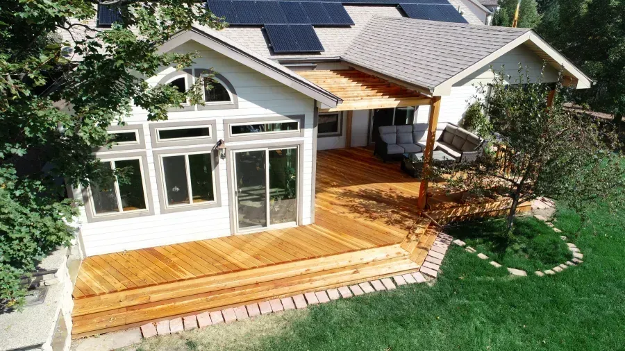 Backyard house with a wooden deck, sliding glass doors, and solar panels on the roof