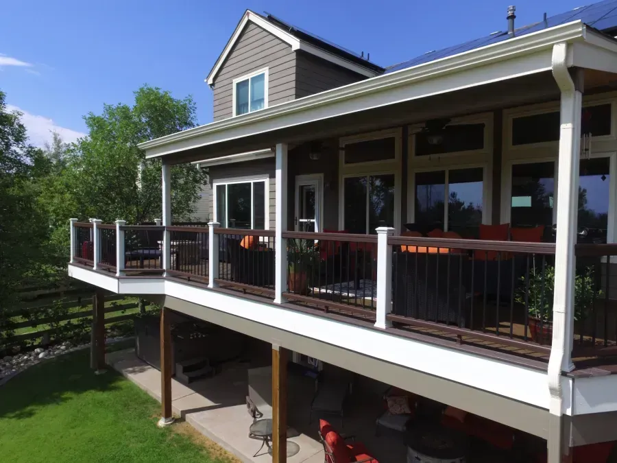 Two-story house with a large wraparound porch and black railings overlooking a green yard