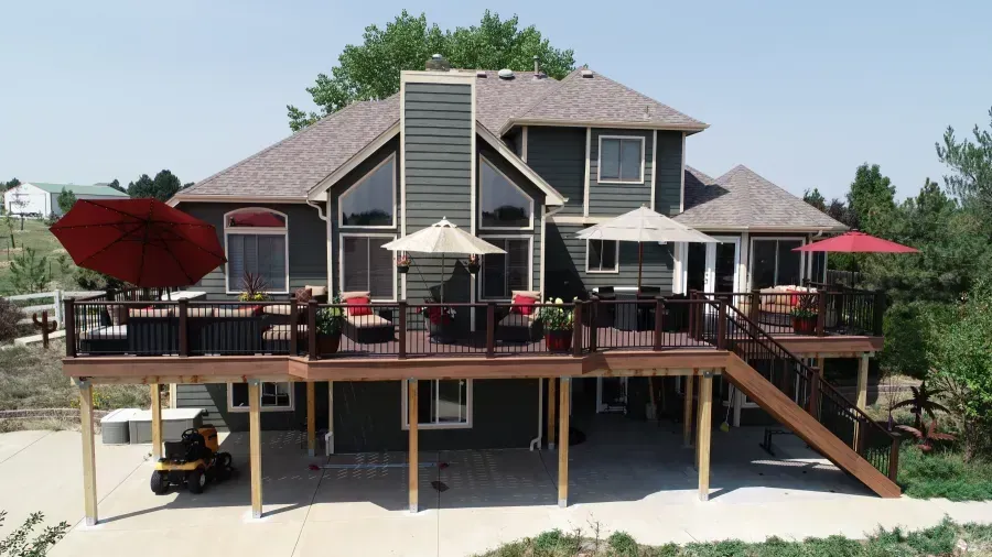 Large gray house with a raised deck, stairs, patio umbrellas, and a golf cart underneath