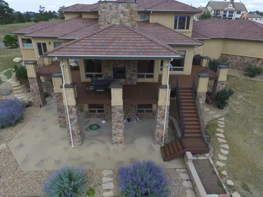 Aerial view of a tan stucco house with stone columns, red tile roof, and exterior stairway