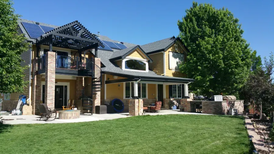 Modern two-story house with solar panels, a large green lawn, and a tree in front.