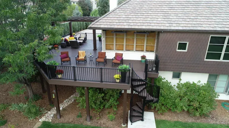 Backyard deck with chairs and a yellow umbrella beside a modern house and stairs