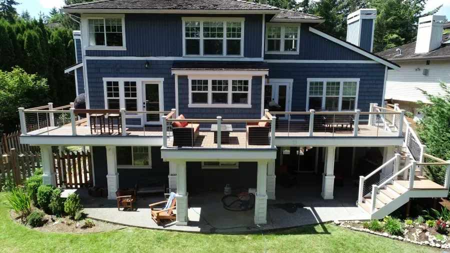 Two-story navy house with a large wooden deck, stairs, and patio seating overlooking a green yard