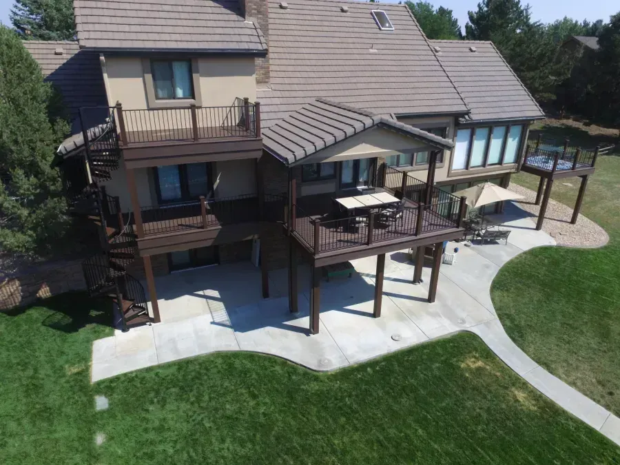 Backyard view of a two-story house with a large wooden deck and curved concrete patio paths