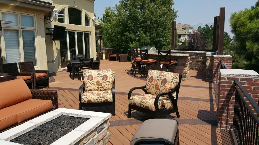 Outdoor patio with orange sofas, patterned chairs, and tables beside a house and brick railing.